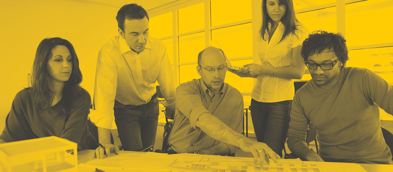 A team of architects reviewing architecture plans on a desk in an office.